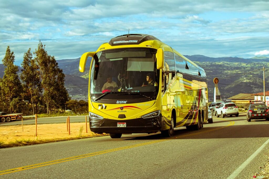 Transporte en Jamaica: guía sobre taxis turísticos y locales A bright yellow bus travels on a scenic mountain road under a blue sky, surrounded by cars and nature.