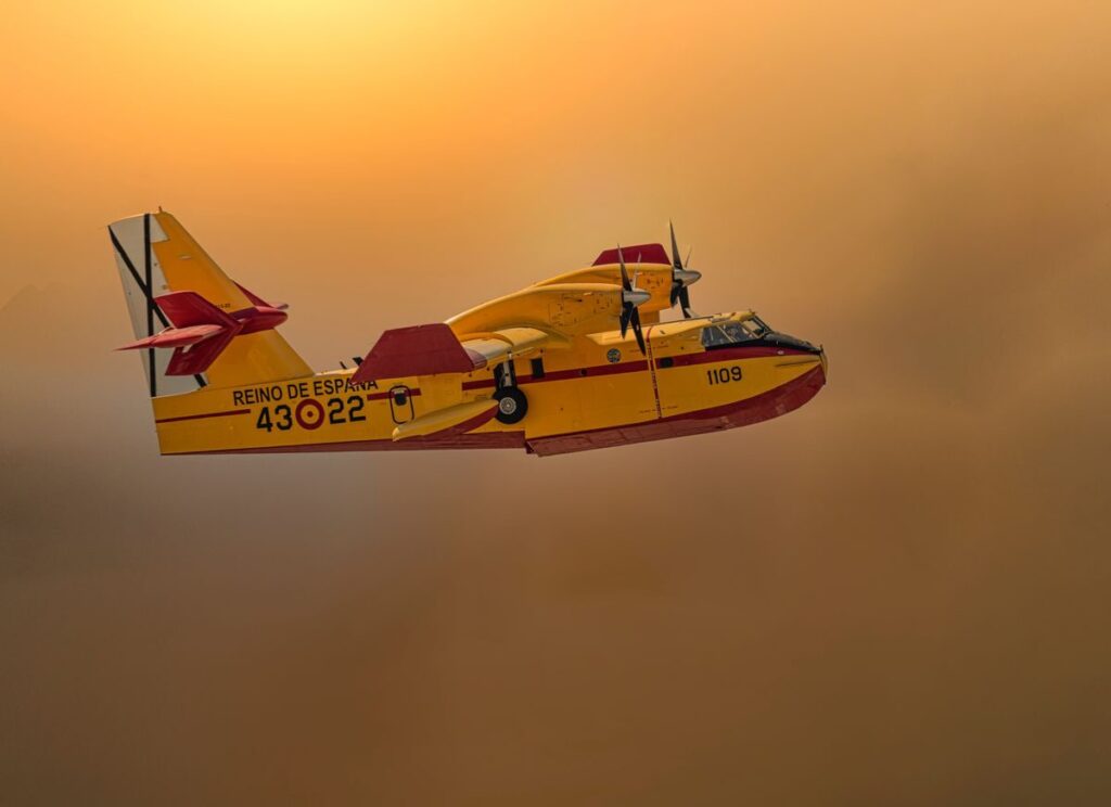 Nuevas rutas al Caribe desde España: 2025 y 2026 A Spanish firefighting plane soaring through a smoky sky at sunset, showcasing aerial firefighting.